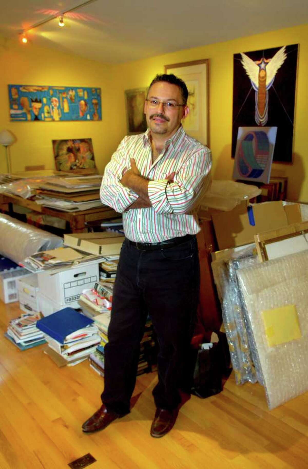 Ben Ortiz poses for a photo surrounded by his library of books and artwork stored in the studio on his property in Ridgefield. Ortiz is curating four art shows simultaneously in September.