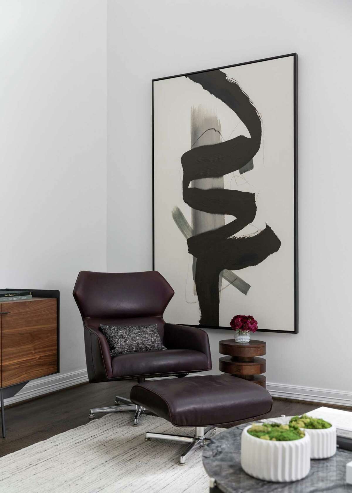 One corner of the living room has a deep burgundy chair and ottoman in front of a large-scale abstract painting.