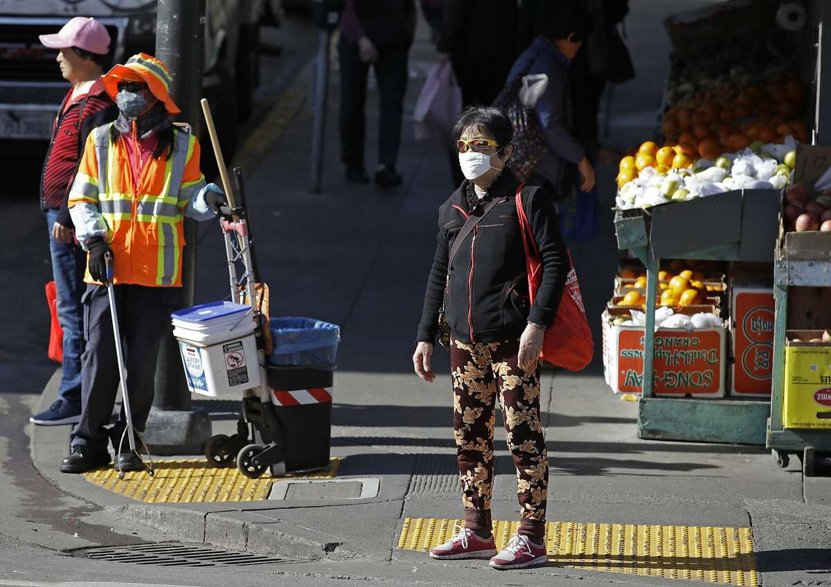 A masked worker and shopper wait for a street signal Friday, Jan. 31, 2020, in the Chinatown district in San Francisco. As China grapples with the growing coronavirus outbreak, Chinese people in California are encountering a cultural disconnect as they brace for a possible spread of the virus in their adopted homeland.
