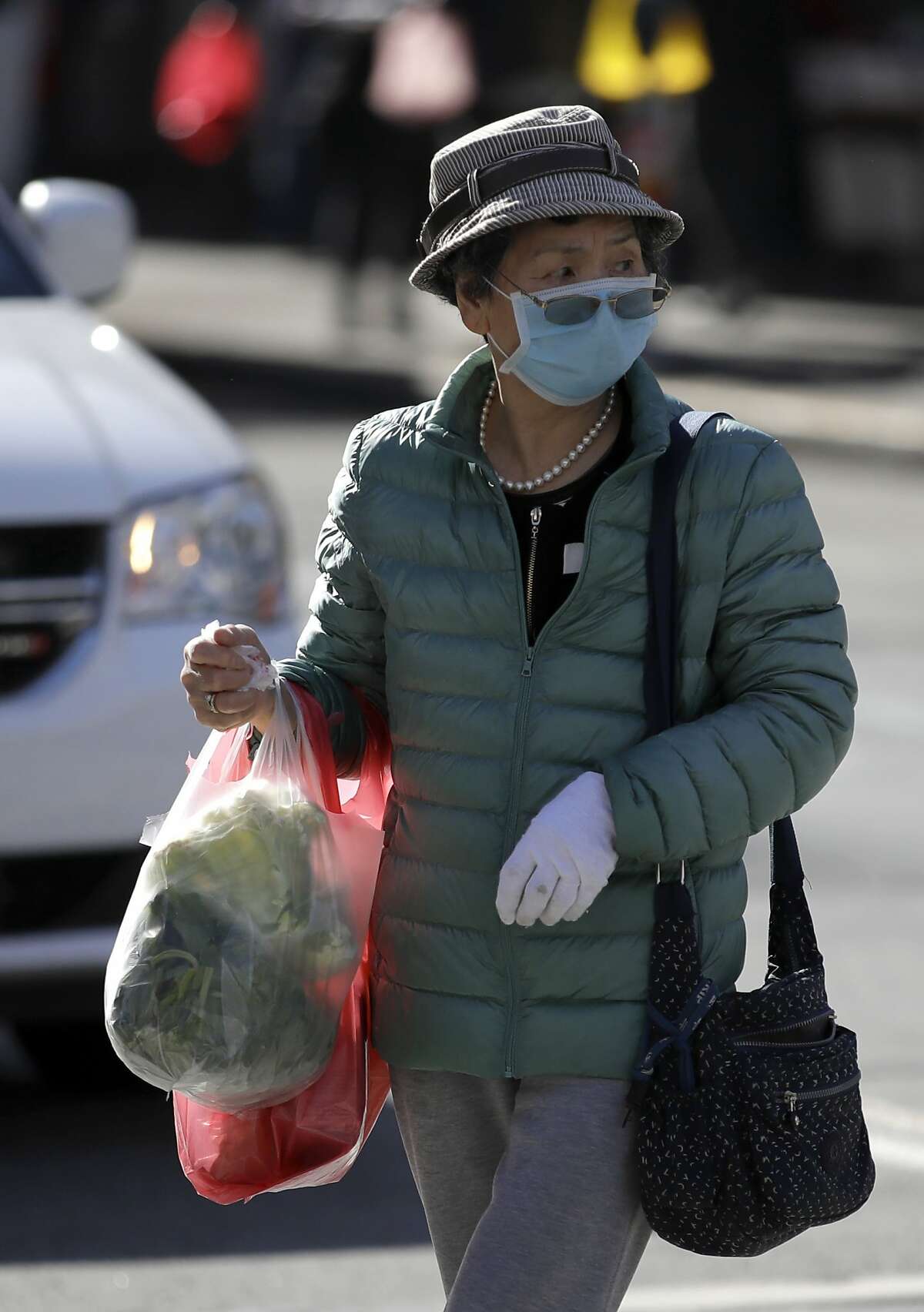 A masked shopper walks across a street Friday, Jan. 31, 2020, in the Chinatown district of San Francisco. As China grapples with the growing coronavirus outbreak, Chinese people in California are encountering a cultural disconnect as they brace for a possible spread of the virus in their adopted homeland. (AP Photo/Ben Margot)
