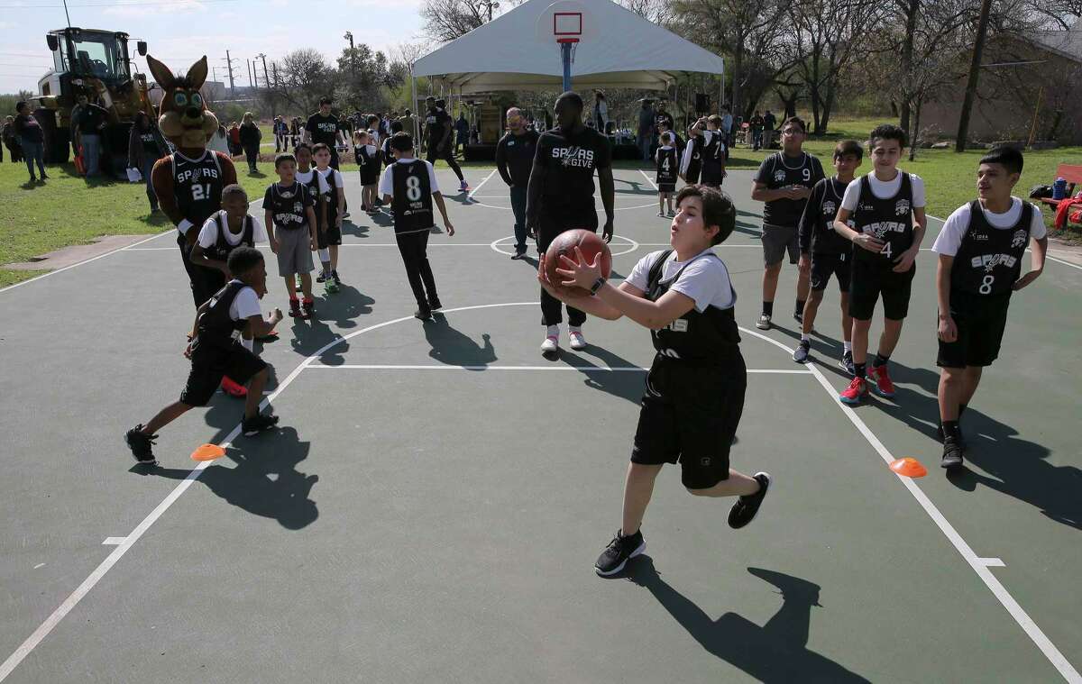 Kids take part in basketball drills on the court Friday at Woodard Park as Spurs star LaMarcus Aldridge, Spurs Sports and Entertainment CEO R.C. Buford, Spurs Sports and Entertainment Chairman Peter J. Holt and Mayor Ron Nirenberg gather with other officials to announce a $1 million initiative to improve the city’s parks. Aldridge is contributing another $100,000 to the program.