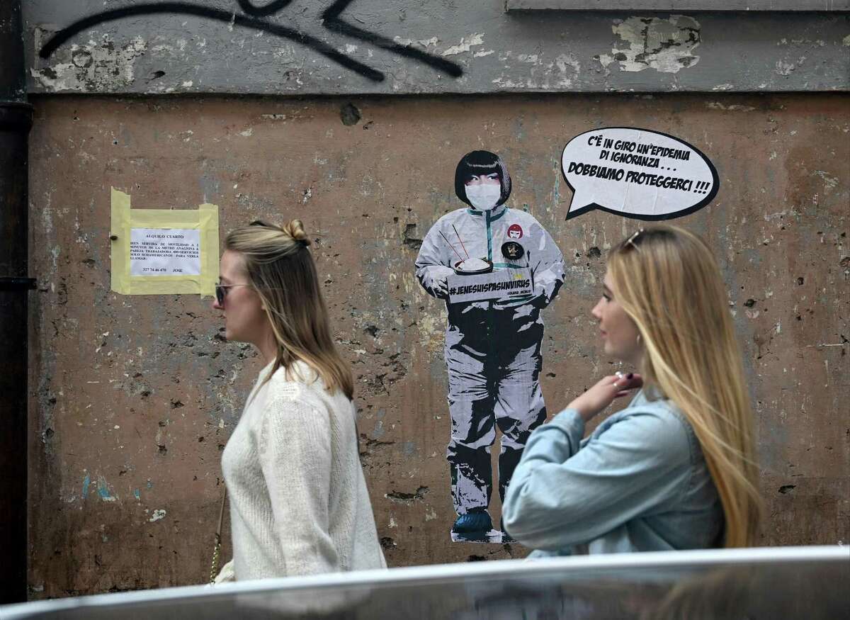 Two women walk by a mural painting reading “There’s an epidemic of ignorance in the air, we must protect ourselves!” referring to the coronavirus outbreak by the street artist Laika near the Chinese district in Rome, on February 4, 2020.