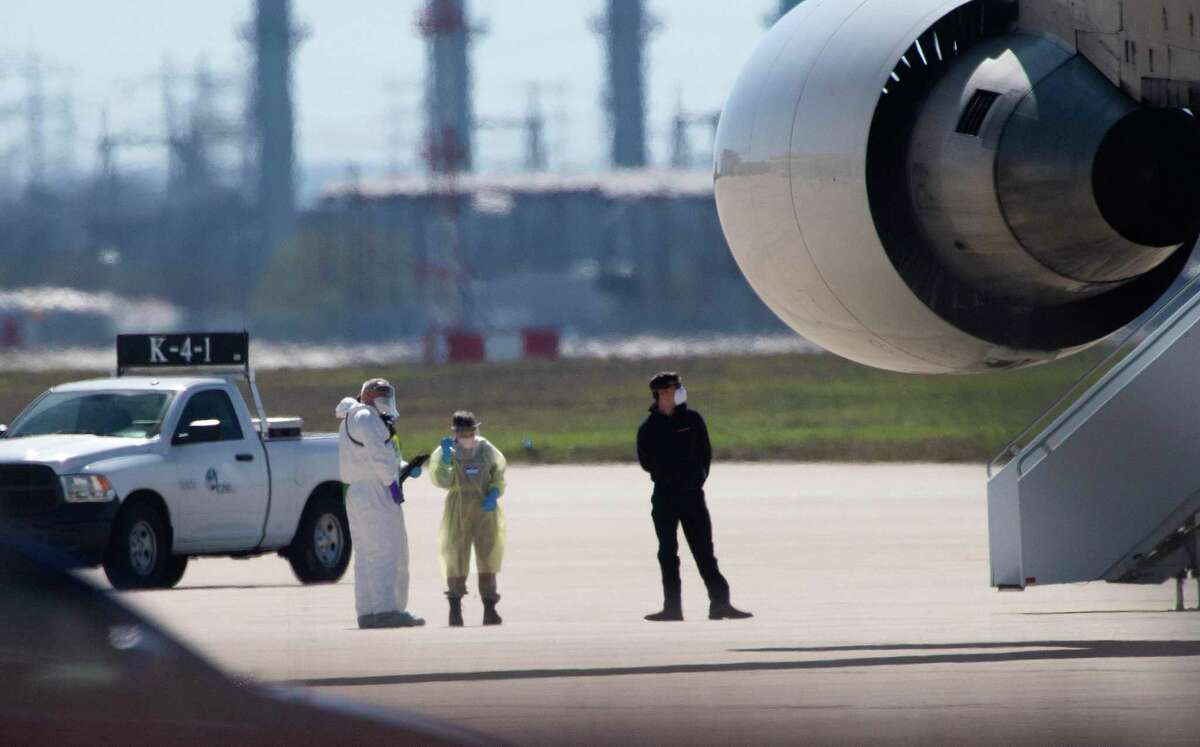 Personnel in hazmat suits wait for people at risk of carrying the coronavirus to disembark from a chartered Boeing 747 at Joint Base San Antonio-Lackland on Friday, Feb. 7, 2020.