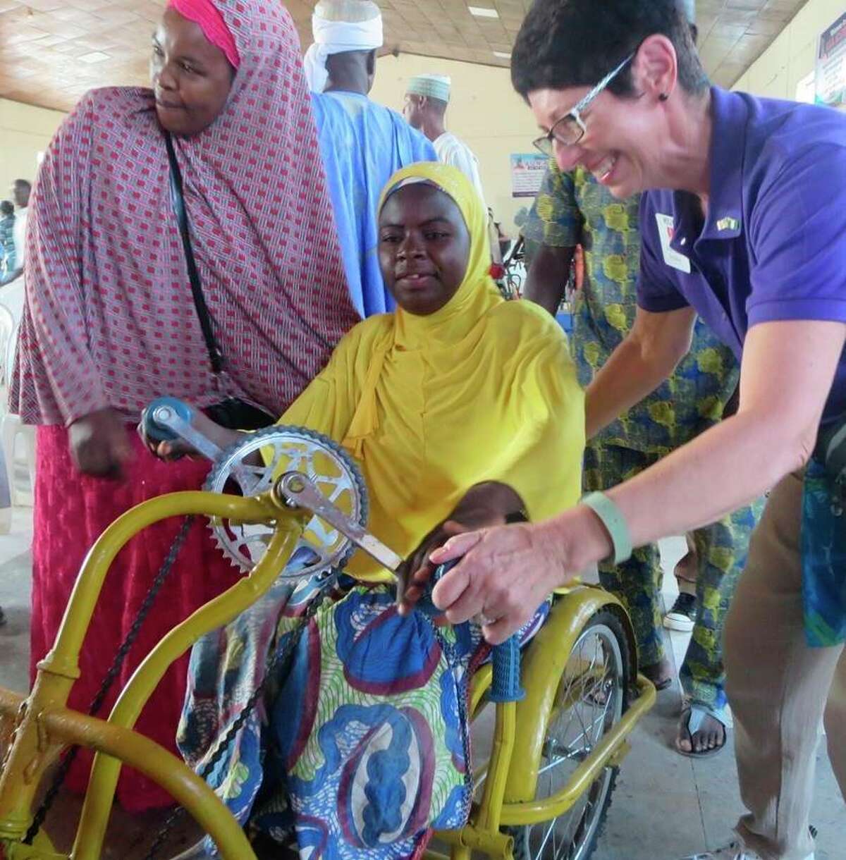 Wheelchair recipient is assisted into her new wheelchair by a Rotarian and her friend at a wheelchair distribution ceremony in Jos Nigeria. (Courtesy Photo)