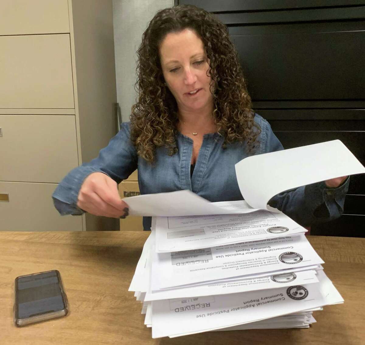 Tara Cook-Littman, of Fairfield, has researched the golf course and agricultural applications in Connecticut of the controversial pesticide chloropyifos, which is banned in Europe and banned in the United States for most household use. She is shown with files at the offices of DEEP, the state Department of Energy and Environmental Protection.