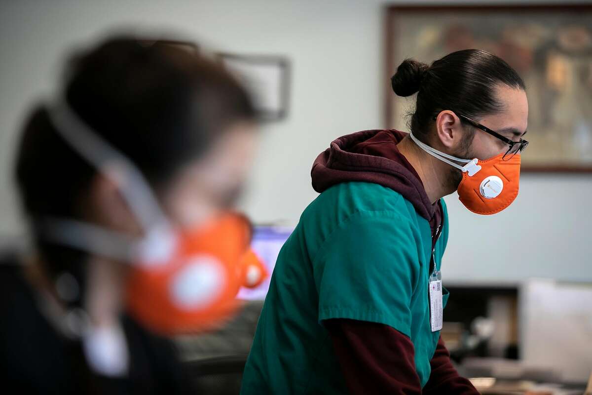 Wearing an N95 face mask, Front Medical Assistant Lead Edwin Moreno, right, mans the front desk at the Foothill Community Health Center on Monday, Feb. 10, 2020 in San Jose, Calif. N95 masks with exhaust valves are not recommended for blocking the spread of the coronavirus