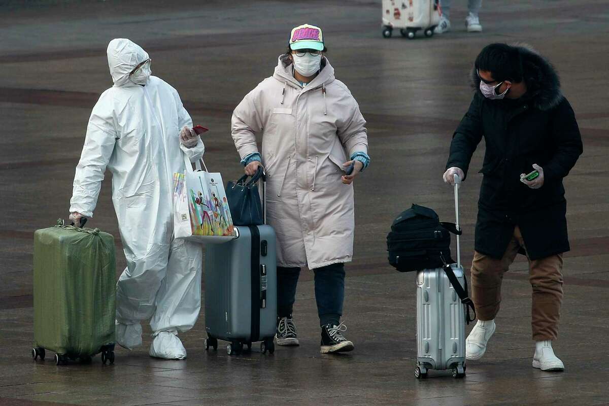 A passenger wearing a full-body protective suit catches the eyes of others as they walk out from the Beijing railway station in Beijing, Tuesday, Feb. 11, 2020. China's daily death toll from a new virus topped 100 for the first time and pushed the total past 1,000 dead, authorities said Tuesday after leader Xi Jinping visited a health center to rally public morale amid little sign the contagion is abating. (AP Photo/Andy Wong)