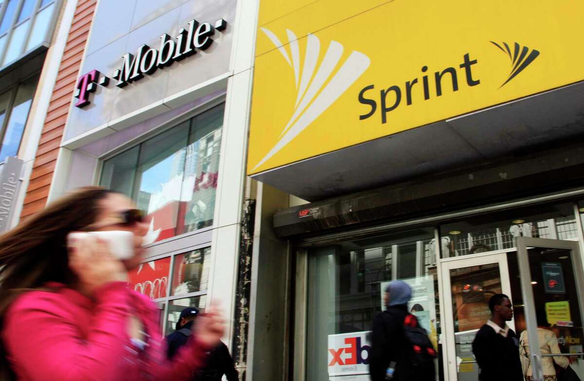 FILE - In this April 27, 2010 file photo, a woman using a cell phone walks past T-Mobile and Sprint stores in New York.