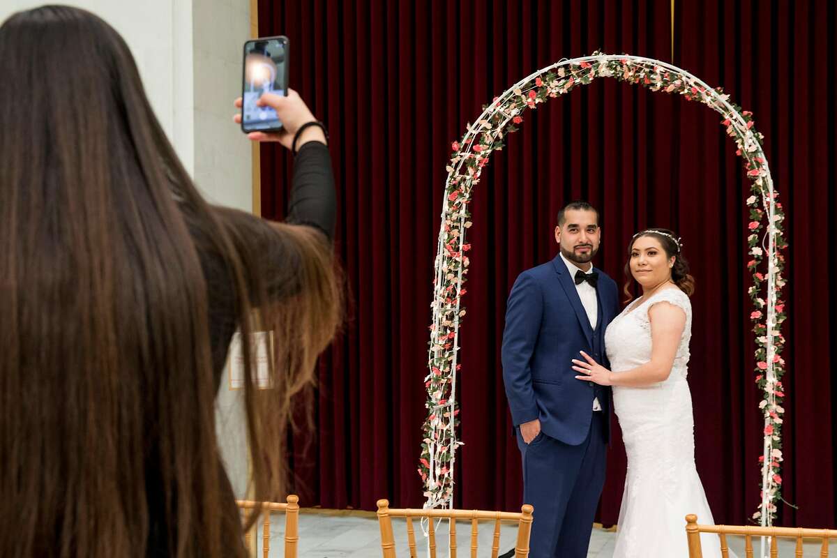 A newly wed couple take pictures under a decorated arch in the North Light Court of San Francisco City hall in San Francisco, Calif. Friday, February 14, 2020. City Hall has hosted their Valentine's Day celebration for four years, with over 140 couples reserved to tie the knot under the rotunda on the romantic date.
