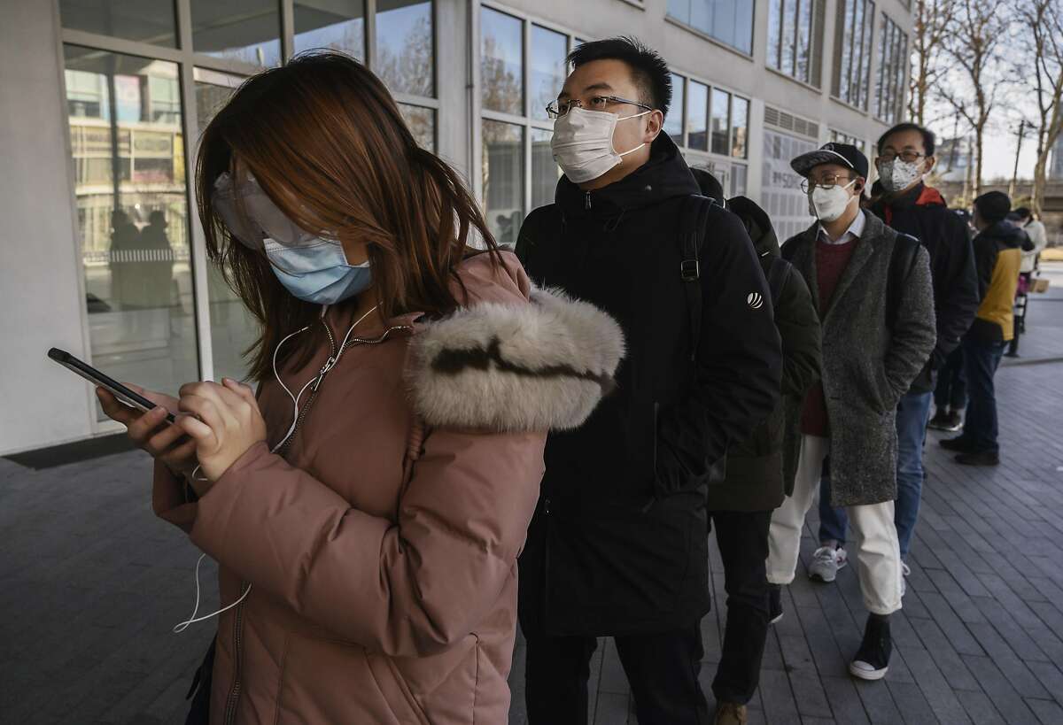 Chinese office workers wear protective masks as they line up to be checked and enter an office building Monday.