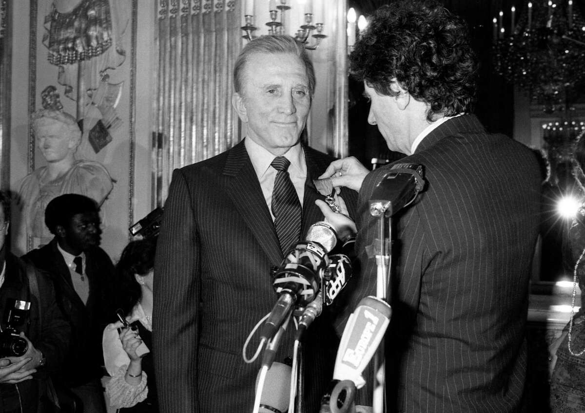 US movie star Kirk Douglas is all smiles as French Culture minister Jack Lang decorated him with the medal of the French Legion of Honor during a ceremony held Friday, March 1, 1985, in Paris. (AP Photo/Lionel Cironneau)