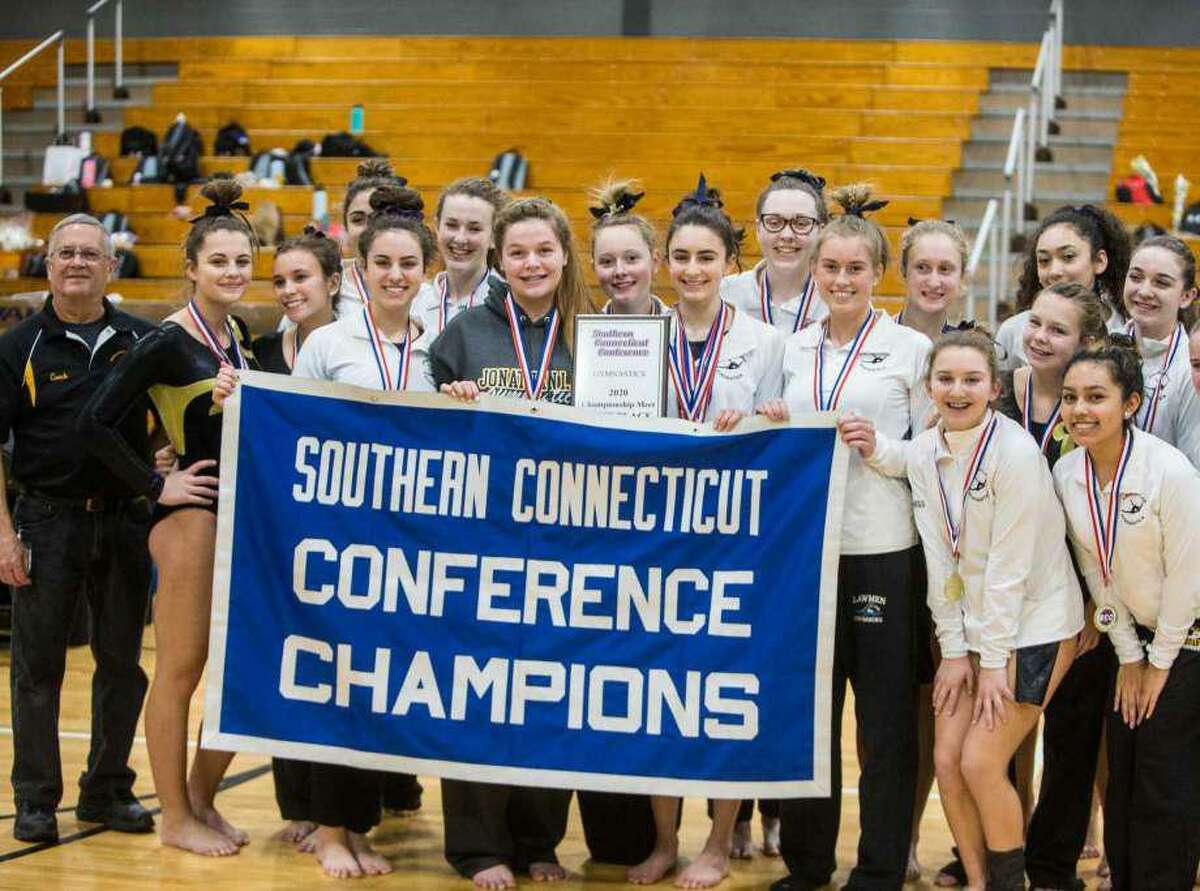 Jonathan Law gymnasts gather together with the banner designating coach Pat Simon's Lady Lawmen as 2020 Southern Connecticut Conference champions.