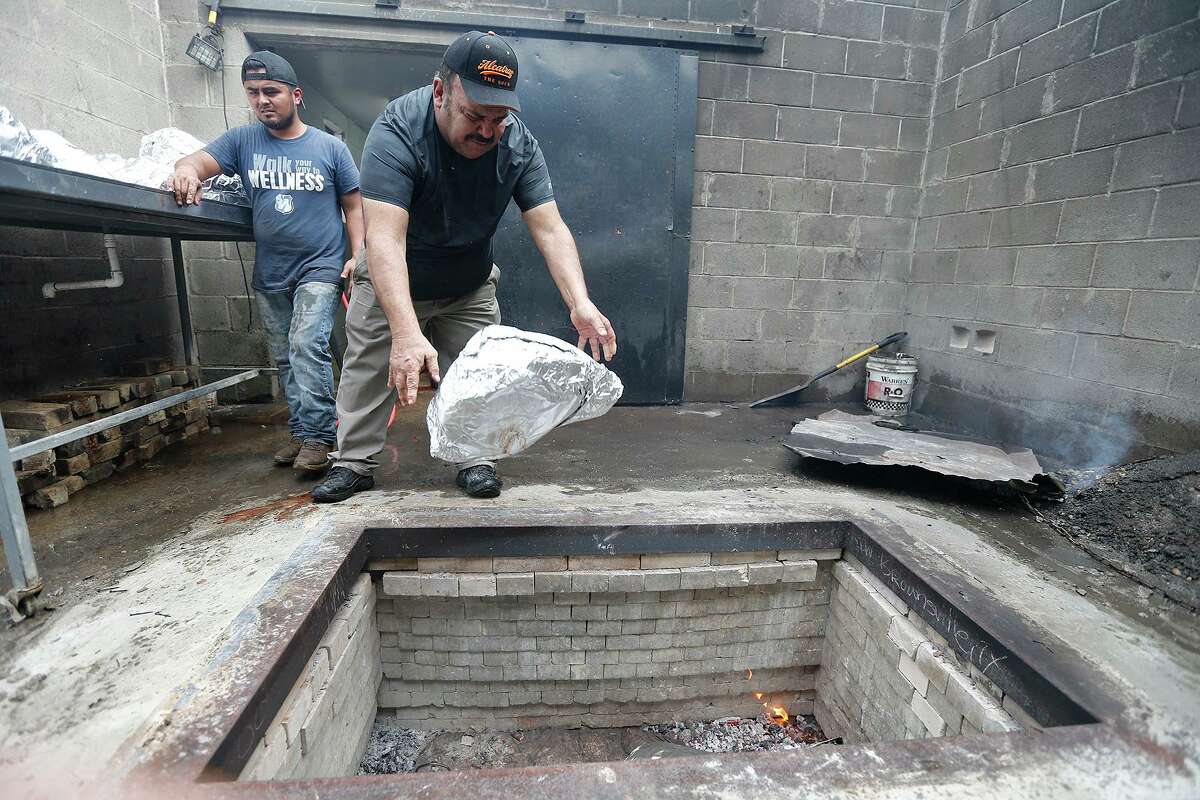 Vera’s Backyard Bar-B-Que employee Arnulfo Antonio, left, and owner Armando Vera put calf heads wrapped in foil into the pit.