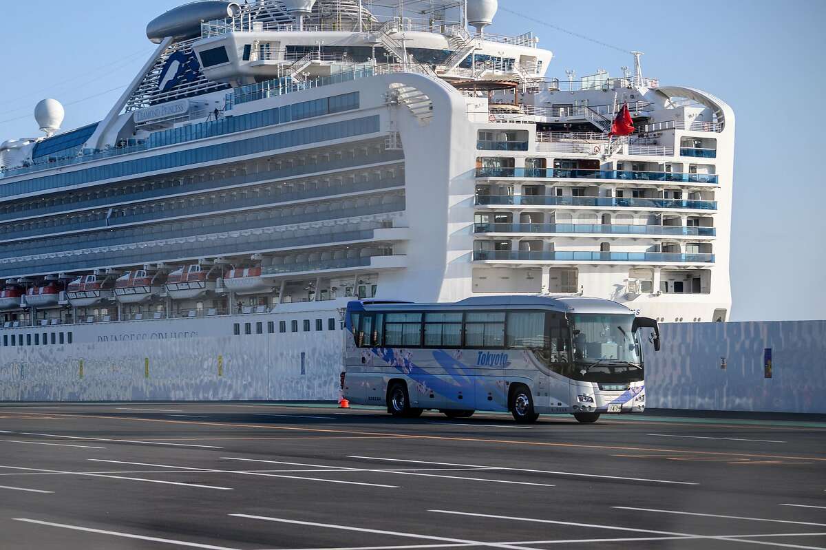A bus drives through dockside past the Diamond Princess cruise ship, in quarantine due to fears of COVID-19 at Daikoku pier cruise terminal in Yokohama, Japan, on Feb, 21, 2020. Hundreds of people have been allowed to leave the ship after testing negative for the disease and many have returned to their home countries to face further quarantine.
