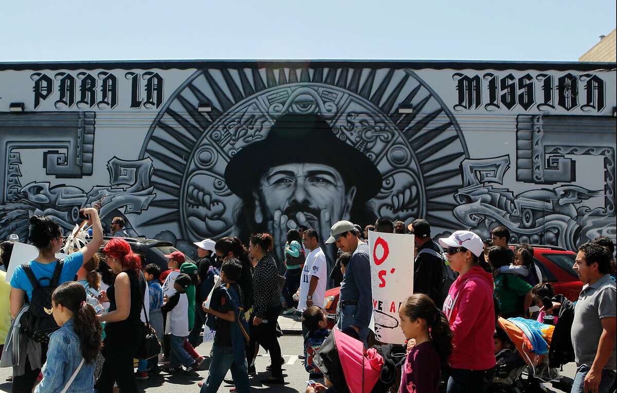 A group of people walk past a mural near the corner of 19th and Mission Streets during the Cesar Chavez Day Parade in the Mission District of San Francisco, Calif. Saturday, April 18, 2015