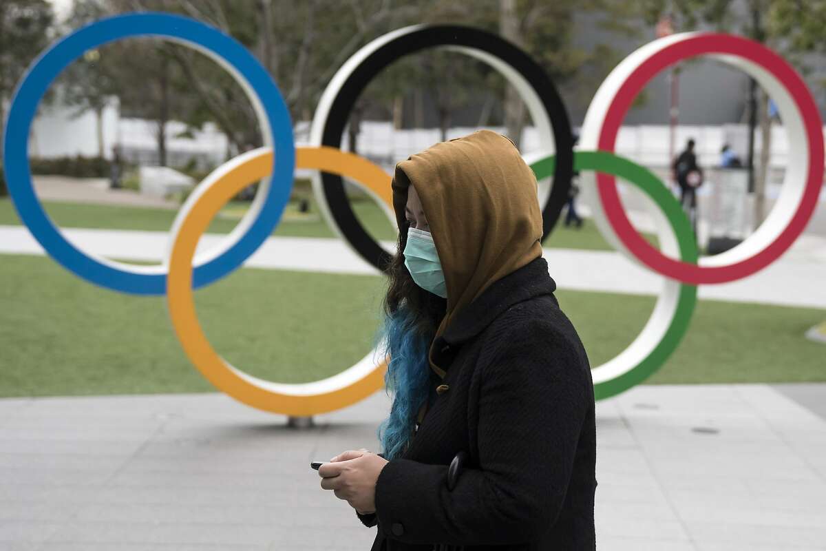A woman wearing a face mask walks past the Olympic rings in front of the new National Stadium, the main stadium for the upcoming Tokyo 2020 Olympic and Paralympic Games.