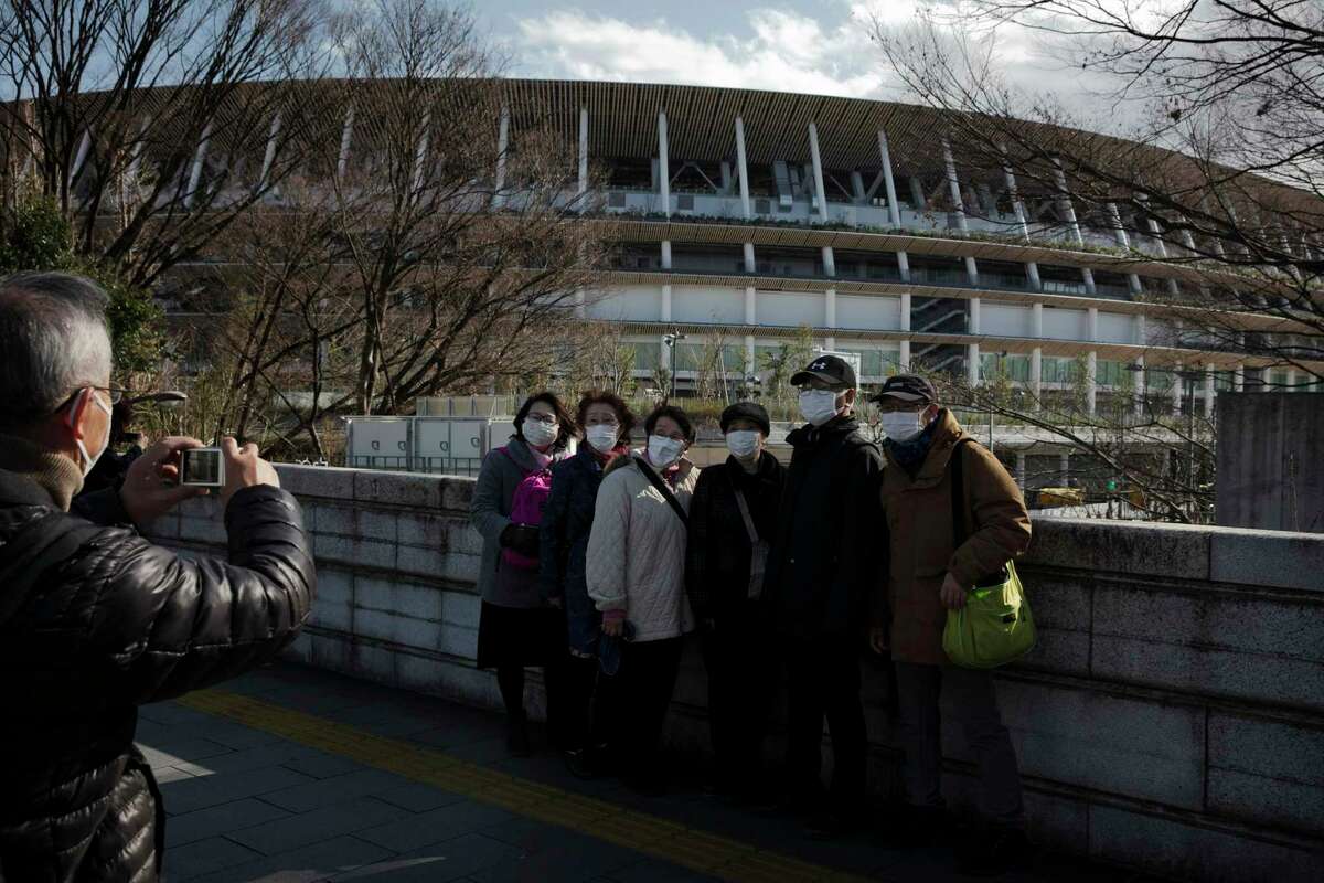 Tourists wear masks as they pause for photos with the New National Stadium, a venue for the opening and closing ceremonies at the Tokyo 2020 Olympics, Sunday, Feb. 23, 2020, in Tokyo. (AP Photo/Jae C. Hong)