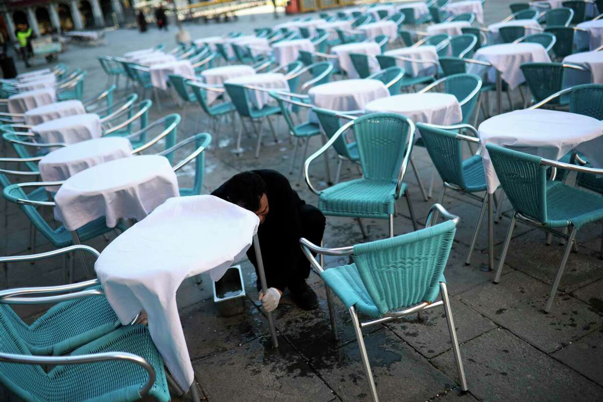 A waiter cleans tables and chairs in an empty restaurant terrace at the St. Mark's Square in Venice, Italy, Friday, Feb. 28, 2020. Authorities in Italy decided to re-open schools and museums in some of the areas less hard-hit by the coronavirus outbreak in the country which has the most cases outside of Asia, as Italians on Friday yearned for a return to normal life even amid fears that the outbreak could plunge the country's economy into recession. (AP Photo/Francisco Seco)