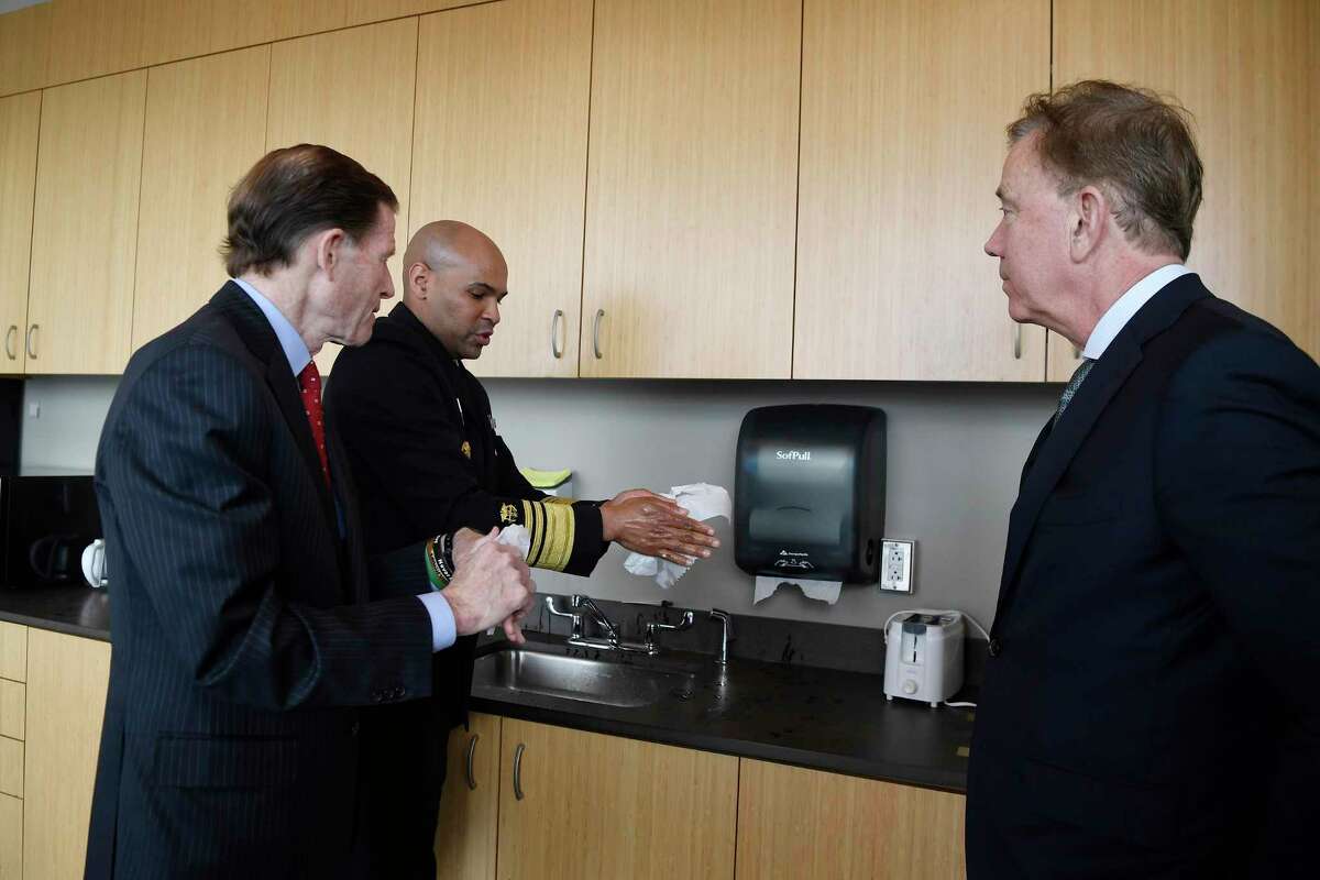 U.S. Surgeon General Vice Admiral Jerome M. Adams, center, demonstrates to U.S. Senator Richard Blumenthal, left, and Connecticut Gov. Ned Lamont, right, the proper amount of time hands should be washed to prevent the spread of the coronavirus during a visit to the Connecticut State Public Health Laboratory, March 2, in Rocky Hill. (AP Photo/Jessica Hill)