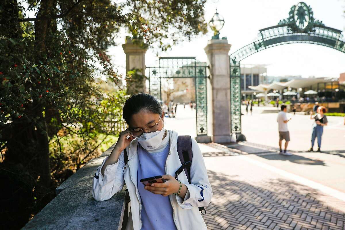 Student Joy Li wears a mask as she reads about the coronavirus on her phone on the UC Berkeley campus on March 4, 2020.