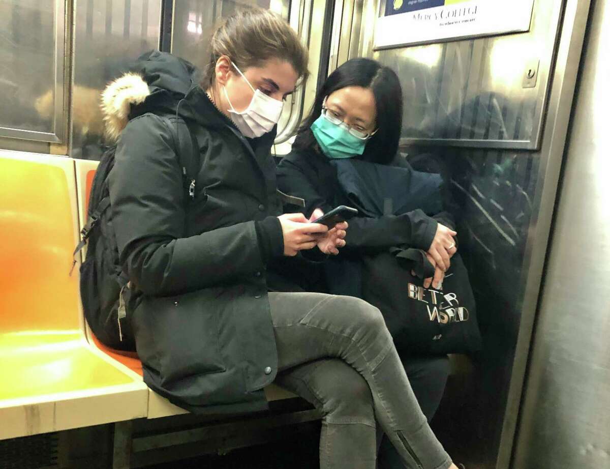 In this March 4, 2020 photo, two women wear masks as they ride a subway train, in New York. Two more cases of the new coronavirus have been confirmed in New York City, raising New York state's total to 13, Mayor Bill de Blasio said Thursday. (AP Photo/Richard Drew)
