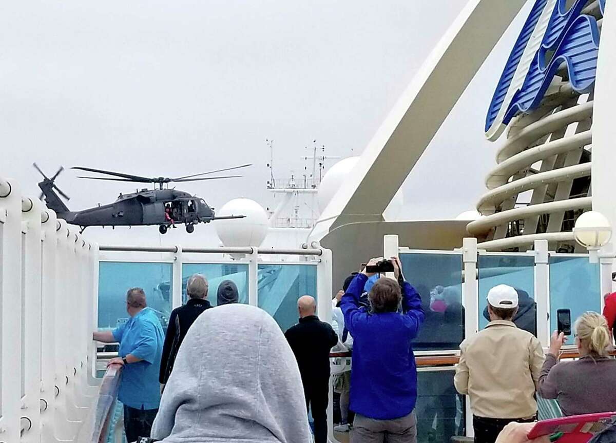 In this photo provided by Michele Smith, passengers look on as a Coast Guard helicopter hovers above the Grand Princess cruise ship Thursday, March 5, 2020, off the California coast. Scrambling to keep the coronavirus at bay, officials ordered a cruise ship with about 3,500 people aboard to stay back from the California coast Thursday until passengers and crew can be tested, after a traveler from its previous voyage died of the disease and at least two others became infected. A Coast Guard helicopter lowered test kits onto the 951-foot (290-meter) Grand Princess by rope as the vessel lay at anchor off Northern California, and authorities said the results would be available on Friday. Princess Cruise Lines said fewer than 100 people aboard had been identified for testing. (Michele Smith via AP)