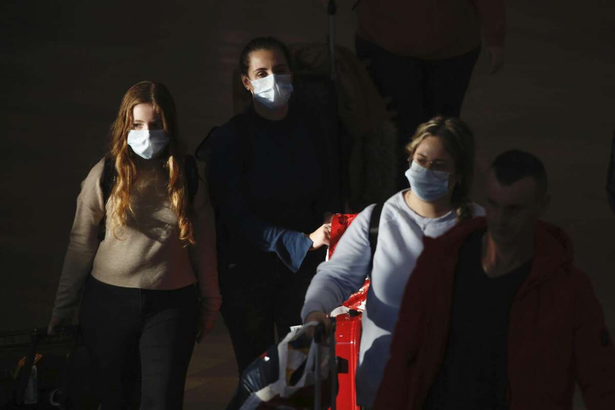 FILE - In this Thursday, Feb. 27, 2020 file photo, travelers wearing protective masks arrive at the Ben Gurion Airport, near Tel Aviv, Israel. A steep drop in business travel could be a gut punch to a tourism industry already reeling from the coronavirus outbreak, as big companies like Amazon try to keep employees healthy by banning trips. (AP Photo/Ariel Schalit, File)