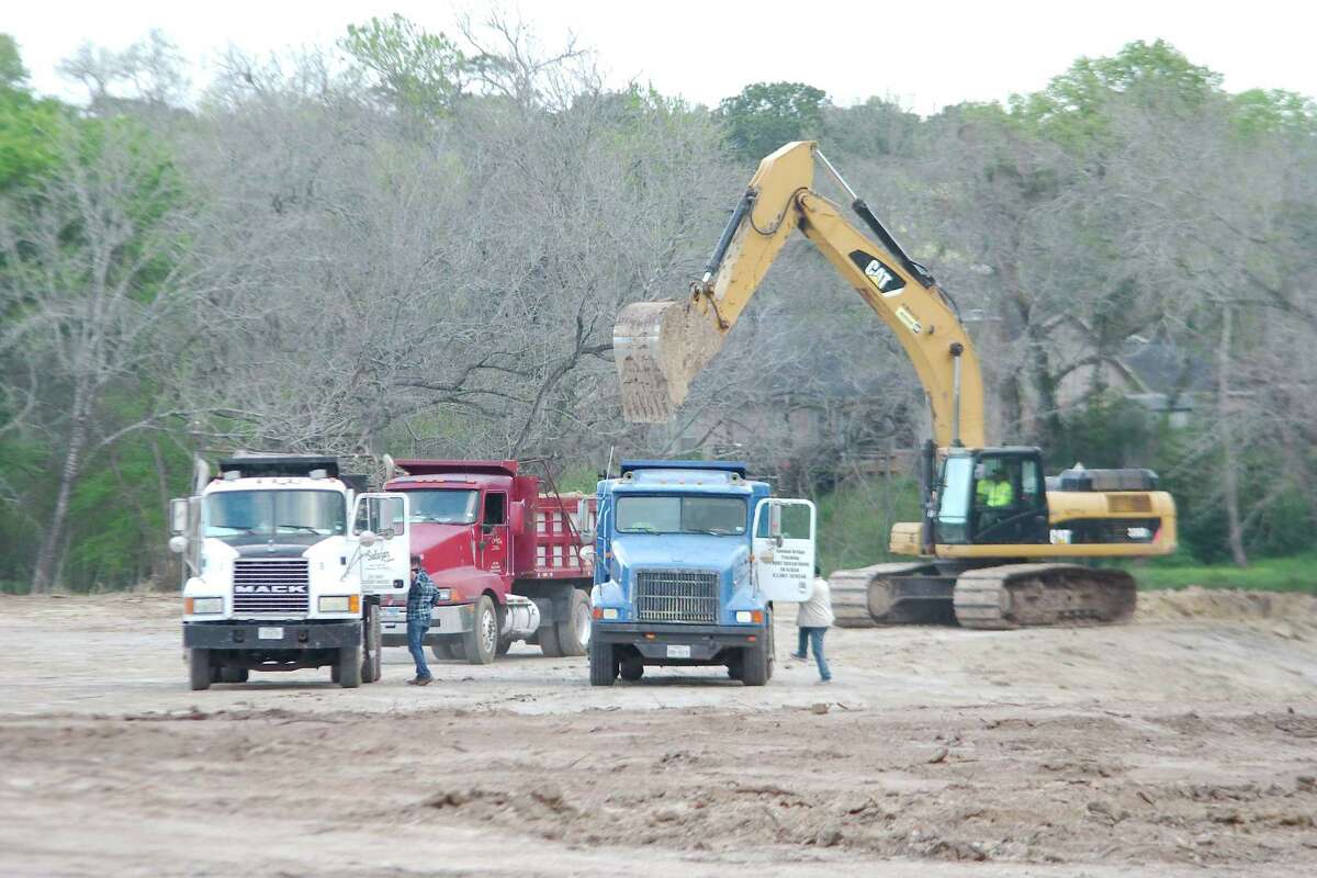 Ttrucks wait for loads at the site of a flood-control project along part of Clear Creek in Friendswood.