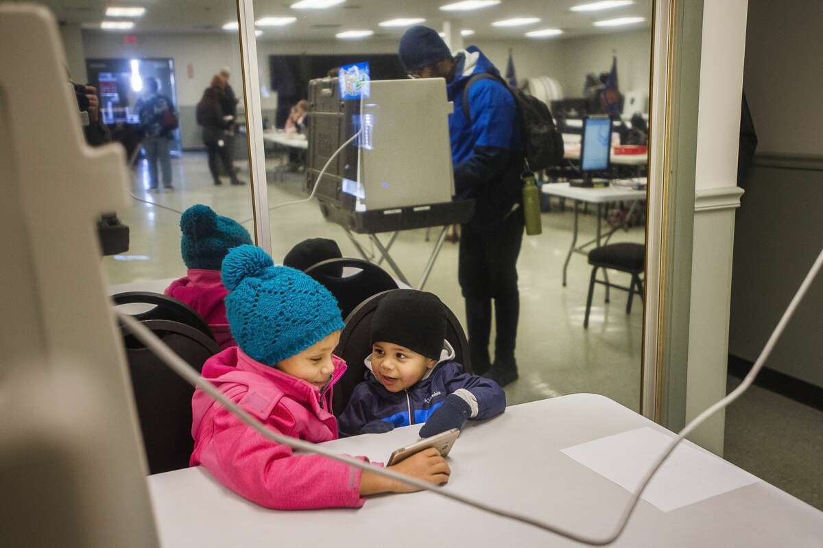 Addison Tryon, 7, and Adrian Tryon, 2, watch a video on their dad's phone as he casts his ballot in the presidential primary election Tuesday, March 10, 2020 at VFW Post 3651. (Katy Kildee/kkildee@mdn.net)