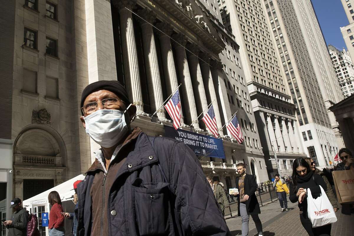 A man wears a mask as he passes the New York Stock Exchange, Monday, March 9, 2020.