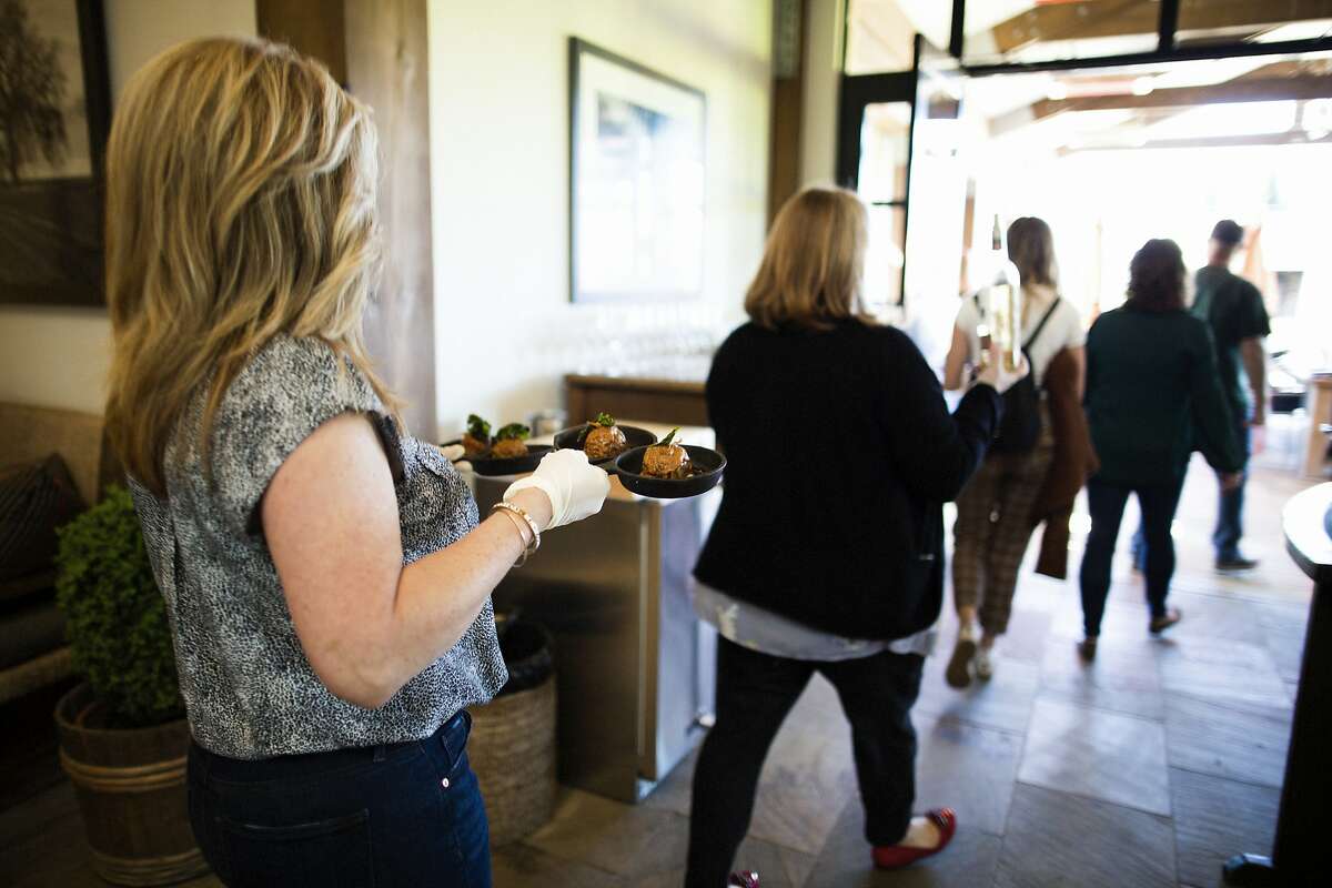 Victoria Acquistapace, wine educator at the Round Pond tasting room wearing gloves as a precautionary measure to protect the spread of the coronavirus as she takes food out to customers at the Round Pond tasting room, Rutherford, California, March 11th, 2020. Napa Valley wineries are seeing a downturn in corporate group visits due to coronavirus concerns. At the same time, these wineries are open for business and are taking extra precautions to be sanitary.