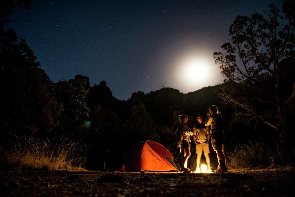 Backpackers talk around a lantern as a full moon rises in the Chisos Basin at Big Bend National Park