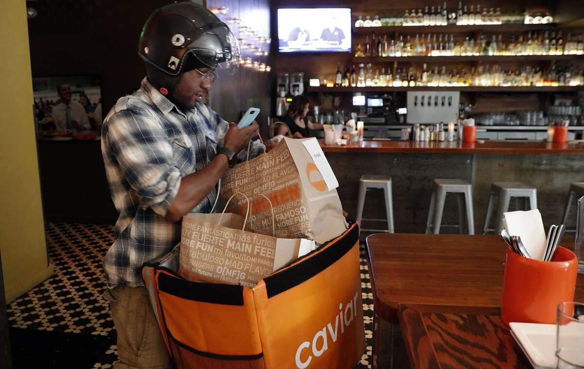 Caviar courier Brandon Whiting checks his order instructions after picking up two orders at Tacolicious in San Francisco, Calif., on Monday, July 24, 2017, where the delivery-only MFChicken restaurant is also prepared and delivered.
