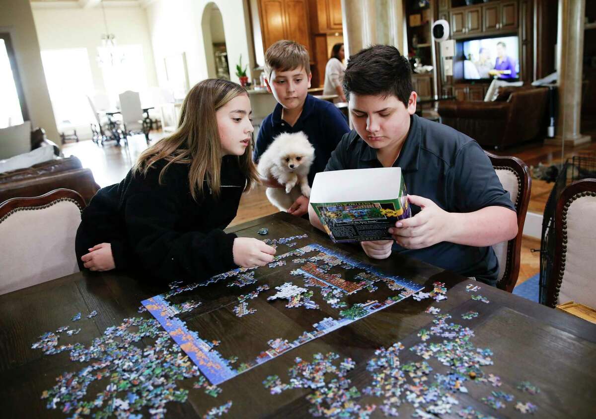 Megan, 12, puppy Coco, Jimmy, 9, and Alex, 15, Goode work on a puzzle in their home as they are self quarantined in their Houston home on Thursday, March 12, 2020.