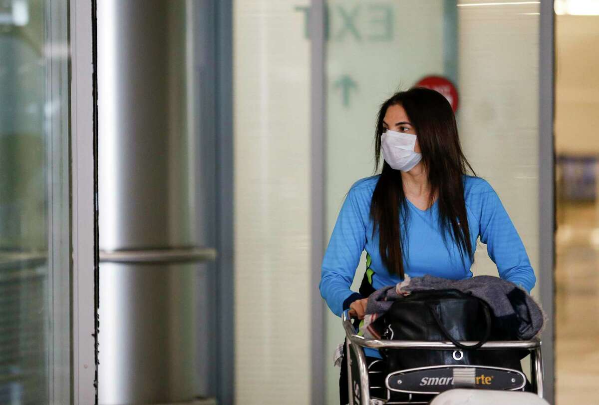 Latika Kohli wears a face mask, as a precaution for the new coronavirus, while exiting the international terminal at George Bush Intercontinental Airport on Thursday, March 12, 2020, in Houston. President Donald Trump set in place a travel ban for people traveling from countries in the European Union.
