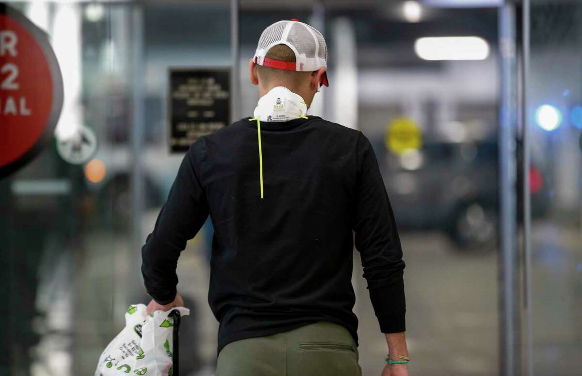 A face mask can be seen wrapped around the back of the neck while exiting the international terminal at George Bush Intercontinental Airport on Thursday, March 12, 2020, in Houston. President Donald Trump set in place a travel ban for people traveling from countries in the European Union.