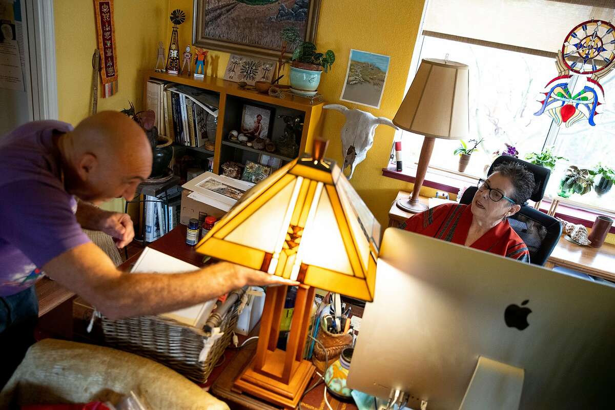 From left: David Stahlberg wipes down his home as Donnee Komisar uses her computer at home on Friday, March 13, 2020, in Cotati, Calif. They recently returned from Italy. Komisar became ill with what her doctor thinks is COVID-19.