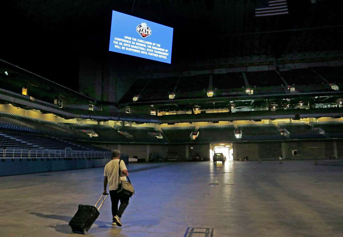 A media member leaves the arena a sign reminds that the rest of the boy's state basketball tournament is postponed, Thursday, March 12, 2020, at the Alamodome in San Antonio. Officials have decided to postpone the tournament after the Thursday afternoon session for Class 3A schools. The University Interscholastic League, which governs extracurricular activities in Texas' public schools, said it made the call due to growing concerns about the COVID-19 virus. (Ron Cortes/The Dallas Morning News via AP)