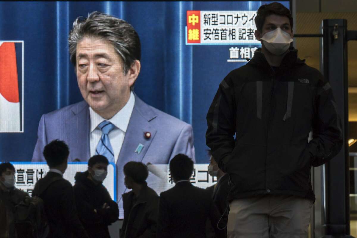 OSAKA, JAPAN - MARCH 14: Pedestrians wearing face masks walk past a monitor showing a live broadcast of a press conference by Japanese Prime Minister Shinzo Abe on Covid-19 on March 14, 2020 in Osaka, Japan. Excluding the Diamond Princess cruise ship cases, the number of coronavirus infections in Japan reached 714 on Saturday as United States President Donald Trump suggested the Tokyo Olympics should be postponed to next year. (Photo by Tomohiro Ohsumi/Getty Images)