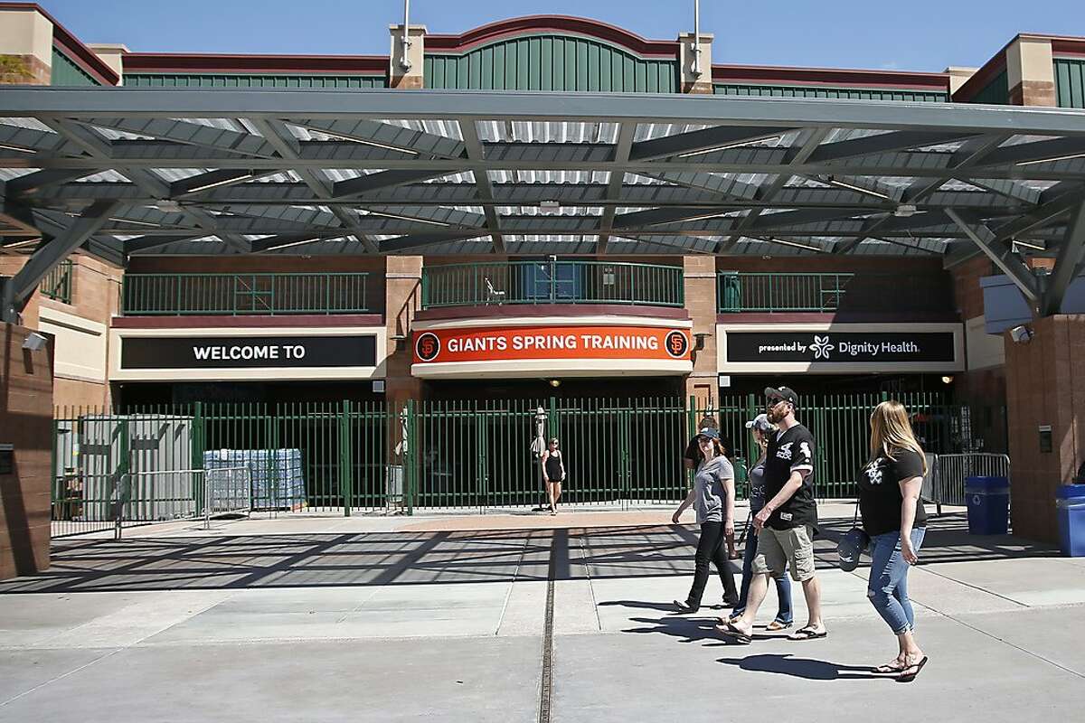 People walk past Scottsdale Stadium, the spring training home of the San Francisco Giants, in Scottsdale, Ariz., Saturday, March 14, 2020. The remainder of spring training baseball games have been canceled due to the coronavirus outbreak. (AP Photo/Sue Ogrocki)