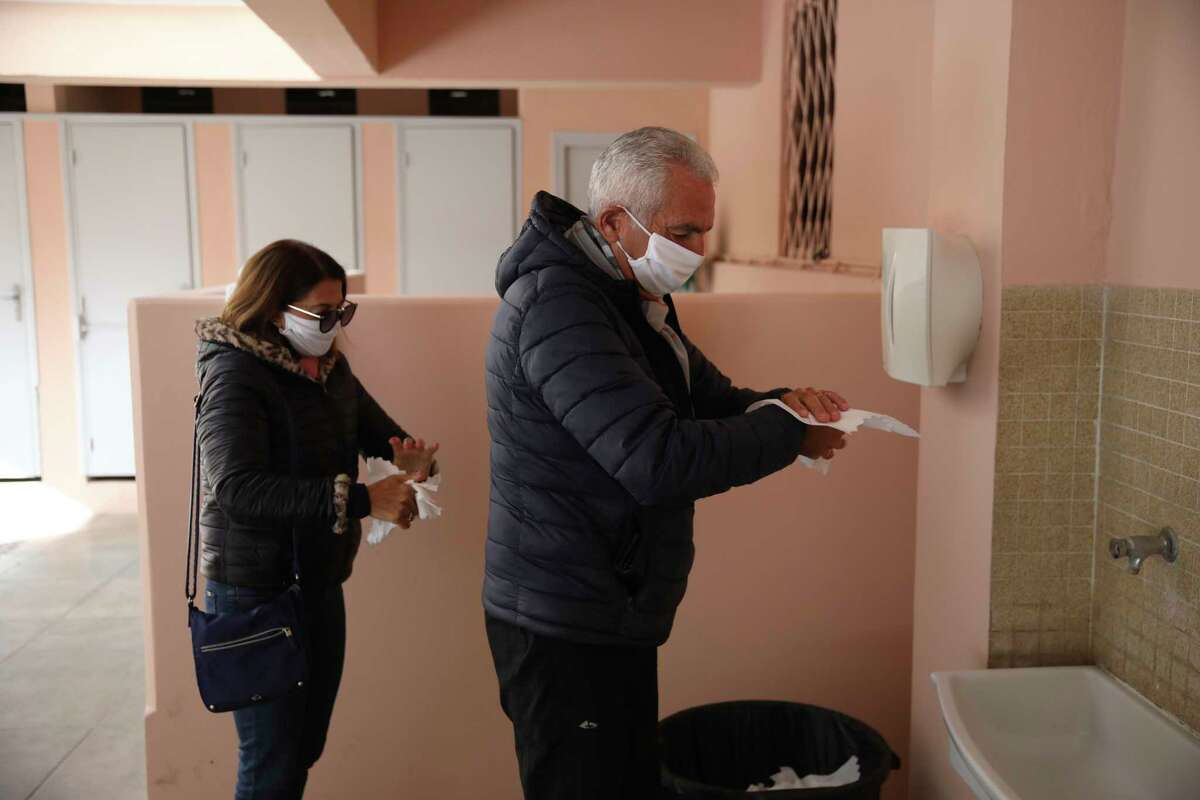 A couple wearing face masks wipe their hands after voting Sunday March 15, 2020 in Menton, southern France. France is holding nationwide elections Sunday to choose all of its mayors and other local leaders despite a crackdown on public gatherings because of the new virus. For most people, the new coronavirus causes only mild or moderate symptoms. For some it can cause more severe illness.