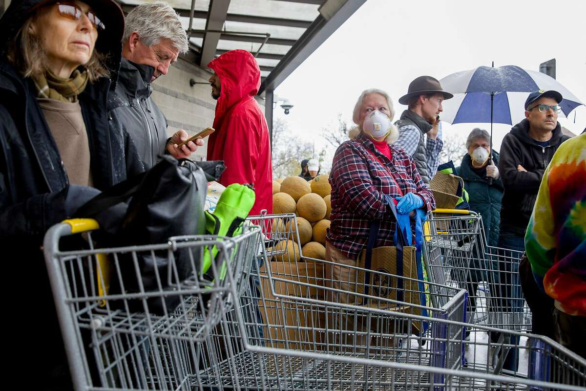 Sam Herbert of Berkeley wears a face mask and gloves as she waits in line with dozens of others to enter Berkeley Bowl in Berkeley Bowl, Calif. Saturday, March 14, 2020. Stores across the Bay Area have been overwhelmed with shoppers "panic buying" amid the thread of the Coronavirus and increased self-isolation within communities.