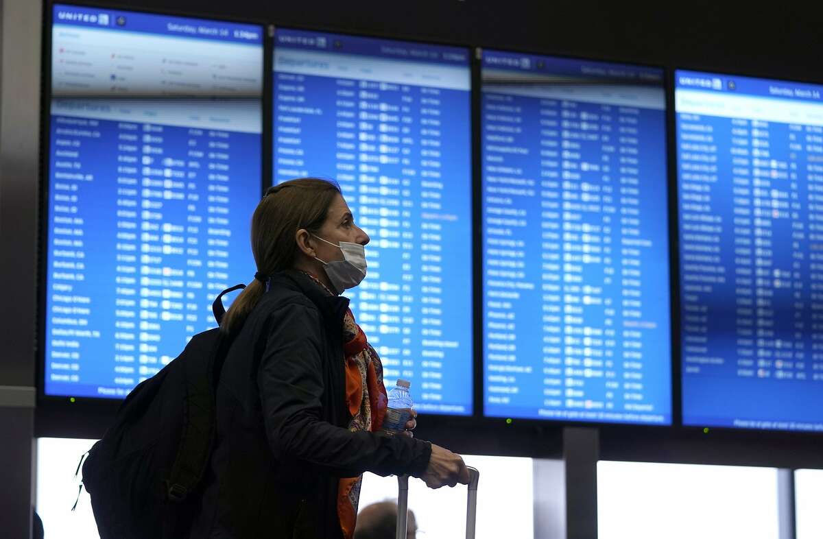 An airline passenger passes by a flight information board at San Francisco International Airport Saturday, March 14, 2020, in San Francisco.  (AP Photo/David J. Phillip)