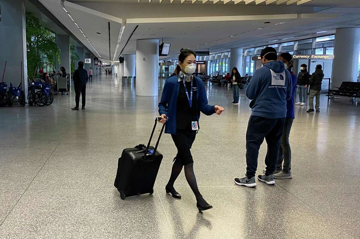 A flight attendant and passengers walk through an SFO corridor. American passengers returning from Europe were surprised to encounter easy clearance through customs and no medical screening for coronavirus, a contrast to some other U.S. airports that reported packed, long lines and screenings.