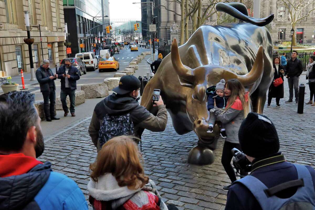 People pose for photos with the Charging Bull statue in New York's Financial District, Sunday, March 15, 2020. New York Gov. Andrew Cuomo. Cuomo said Saturday that more than 600 New Yorkers have been diagnosed with COVID-19, the disease caused by the virus. (AP Photo/Richard Drew)