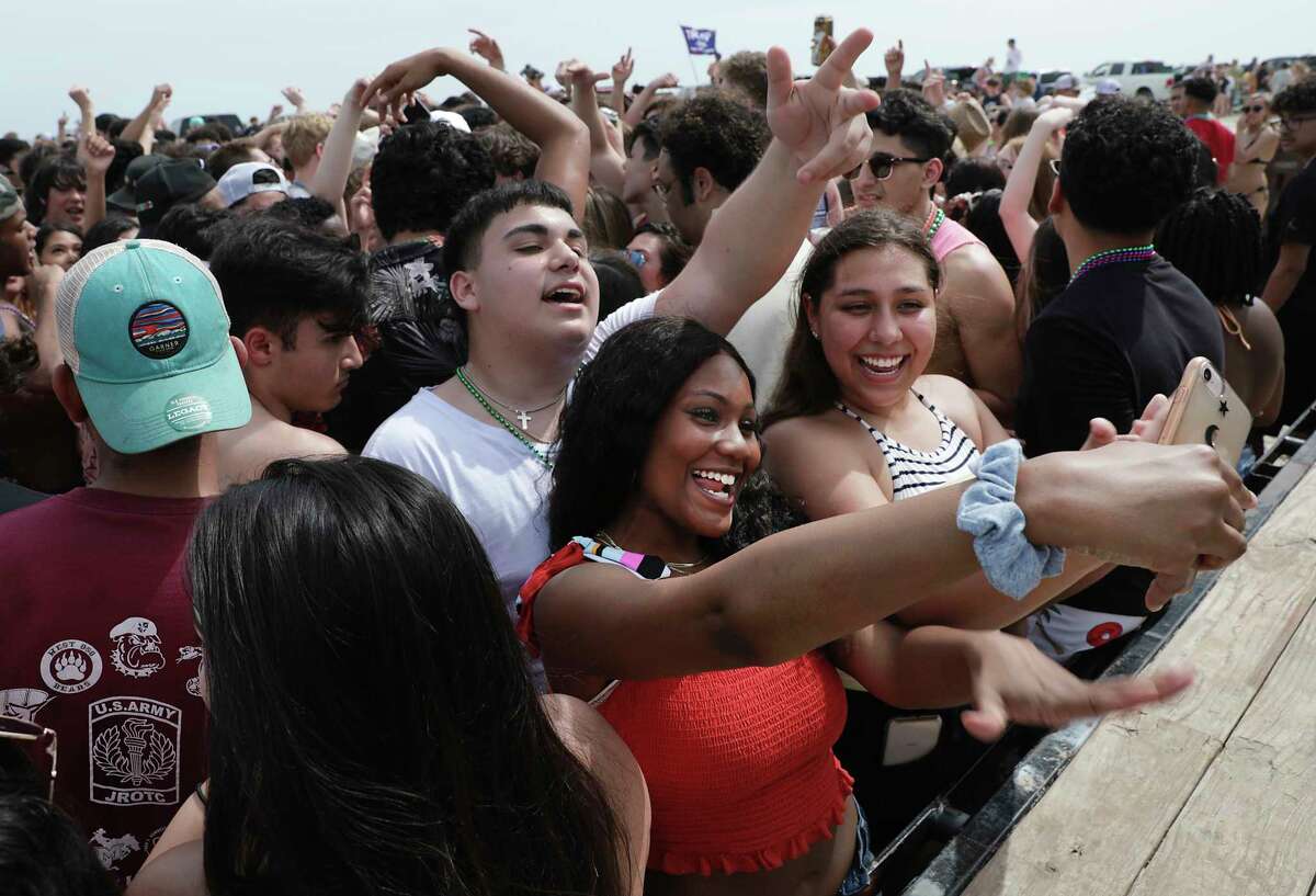 Sabrina Miller, in red, of San Antonio, takes a selfie as a large group of partiers attend a concert on the beach.