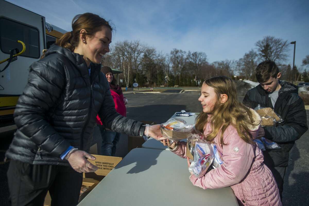 Volunteer Kayla Contardi, left, hands a school lunch to Brooklyn Deisler, 9, Monday, March 16, 2020 at the Greater Midland Community Center. Several Midland Public School school buildings, as well as other designated pick-up locations, will be open for meal pick-up on Monday, Wednesday, and Friday until April 3. (Katy Kildee/kkildee@mdn.net)