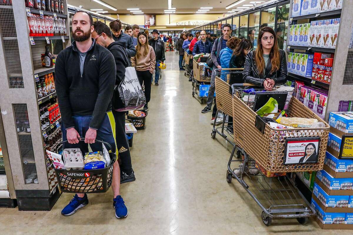Vinny Verdeschi (left) and Liz Roland (right) wait in line at Safeway after Mayor London Breed announced that six Bay Area counties would lockdown non-essential services due to the coronavirus on Monday, March 16, 2020 in San Francisco, California.