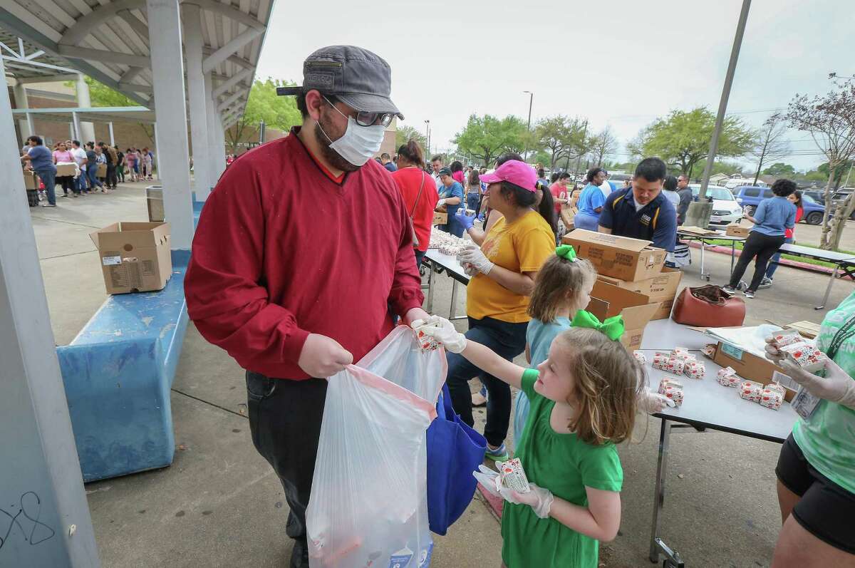 Haryie Garrigues wears a protective mask as he get drinks from 5-year-old Eleanor Hutcheson as the Houston Independent School District along with the Houston Food Bank handed out food to hundreds of families in need Saturday, March 14, 2020, in Houston.