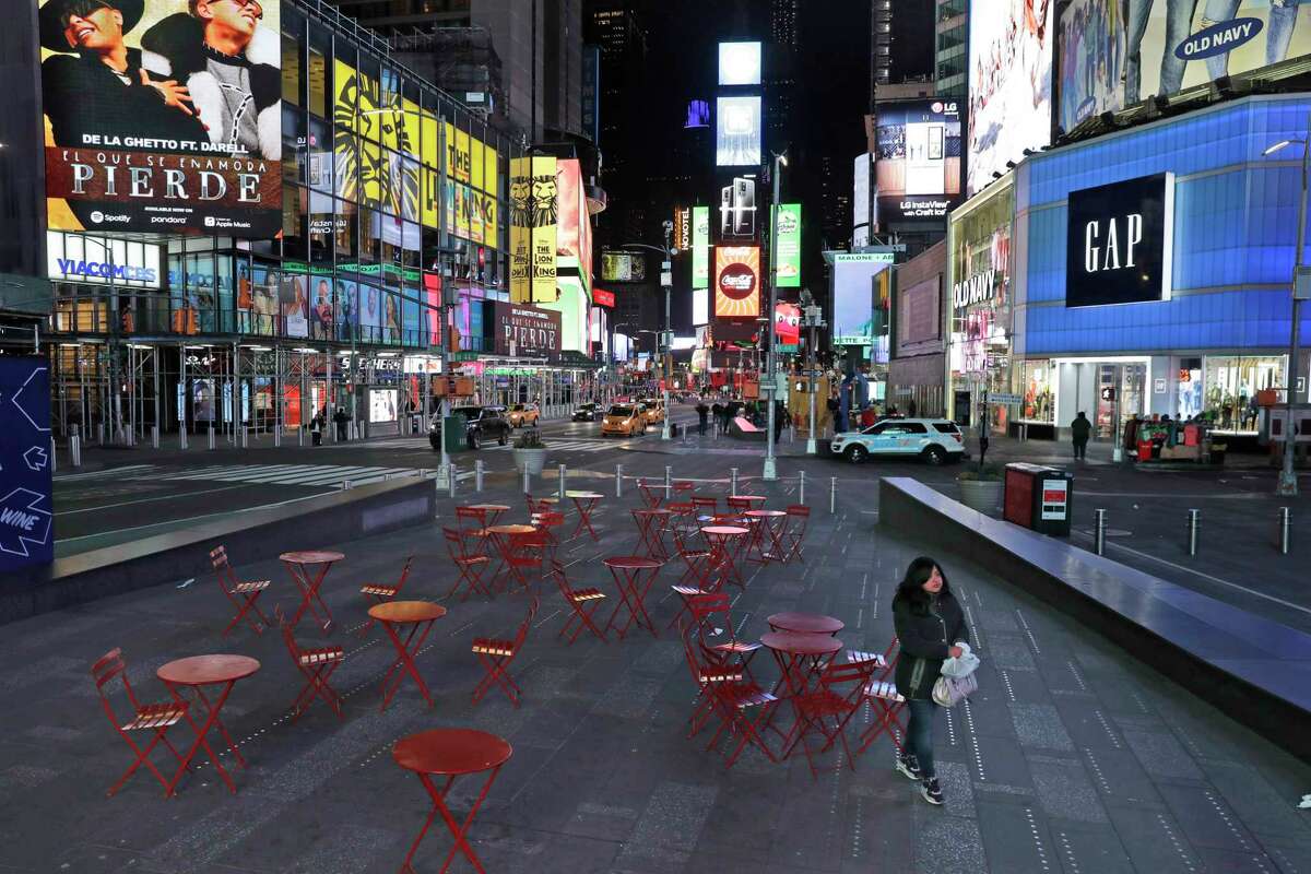 A woman walks through a lightly trafficked Times Square in New York, Monday, March 16, 2020. Bars and restaurants will become takeout-only and businesses from movie theaters and casinos to gyms and beyond will be shuttered Monday night throughout New York, New Jersey and Connecticut because of the coronavirus, the states' governors said.